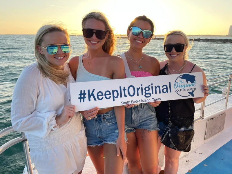 Guests holding a #KeepItOriginal sign aboard The Original Dolphin Watch at sunset